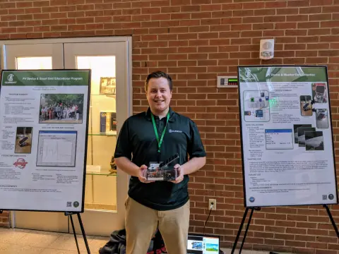 Presenter holding a solar circuit device between posters on PV device education and weather data collection