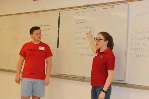 Two presenters at a whiteboard with handwritten Raspberry Pi GPIO Python code