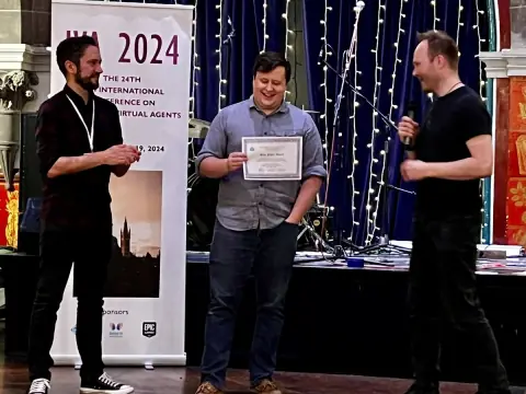 Ian on stage holding a Best Paper certificate beside an IVA 2024 conference banner