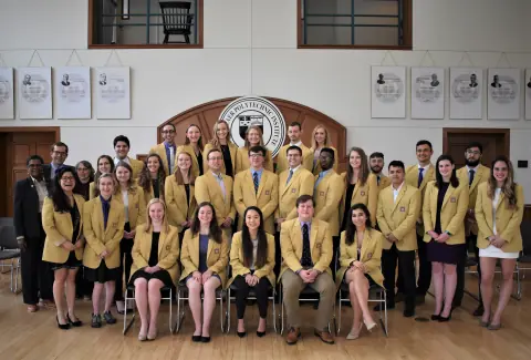 Formal group portrait of about 35 people in matching gold blazers beneath the Rensselaer seal